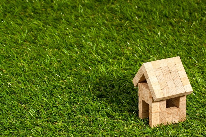 A small wooden toy house sits on a patch of bright green grass.