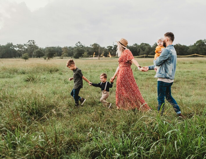 A family walks with their young children through green field